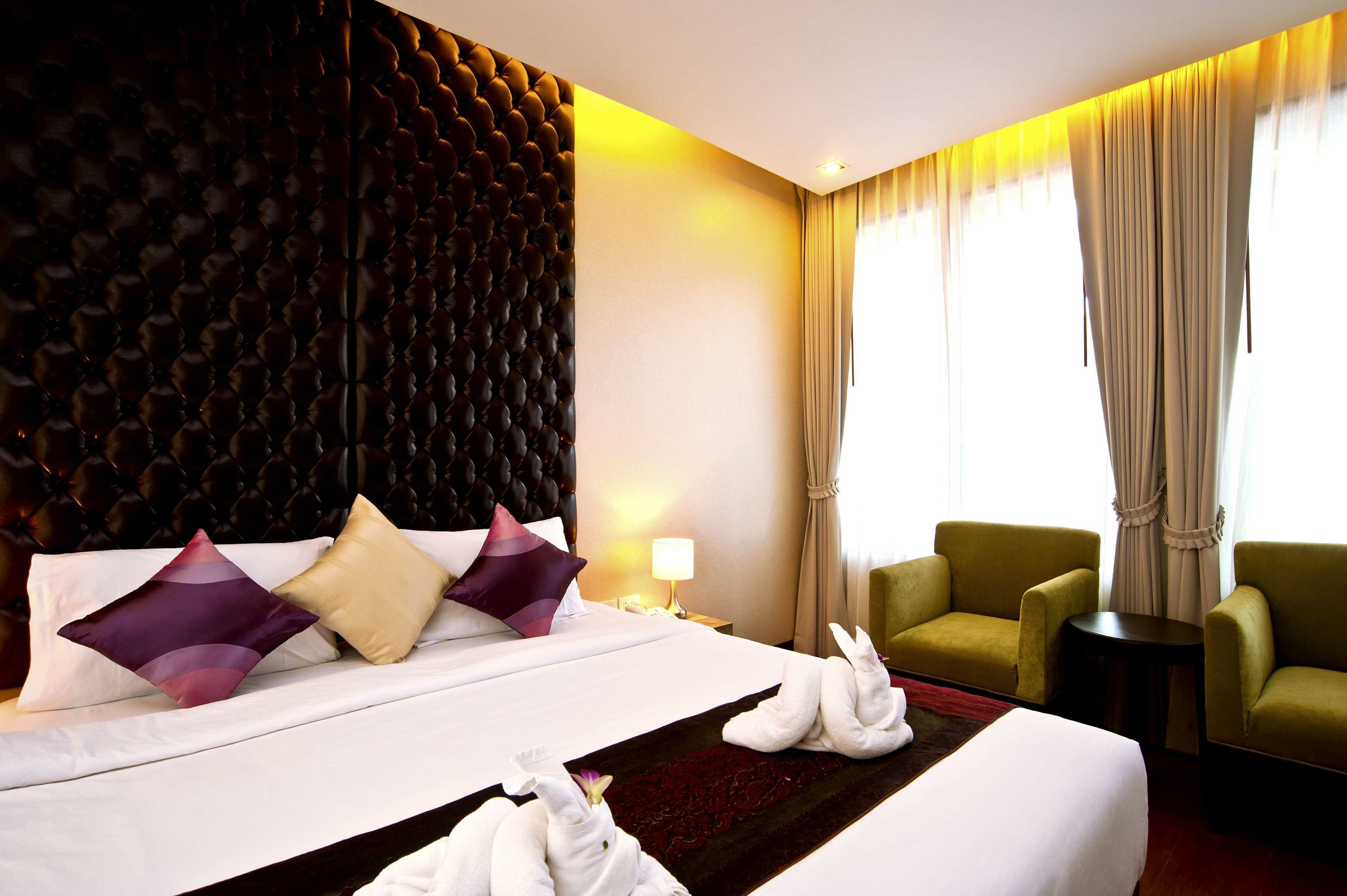 Hotelkamer met een groot bed, twee groene fauteuils, een tafeltje en een decoratief wandpaneel.