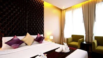 Hotelkamer met een groot bed, twee groene fauteuils, een tafeltje en een decoratief wandpaneel.