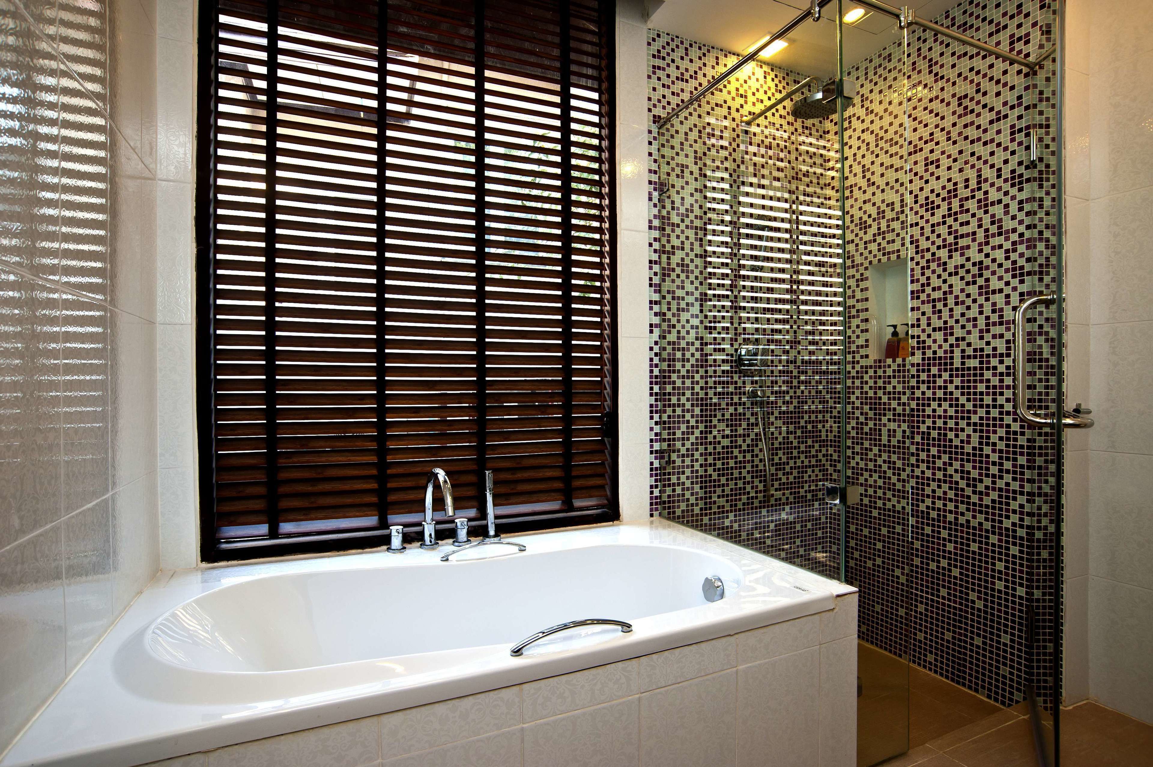 A modern bathroom with a large bathtub, a glass shower enclosure, and a window with blinds.