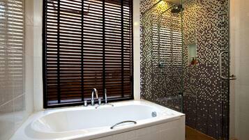 A modern bathroom with a large bathtub, a glass shower enclosure, and a window with blinds.