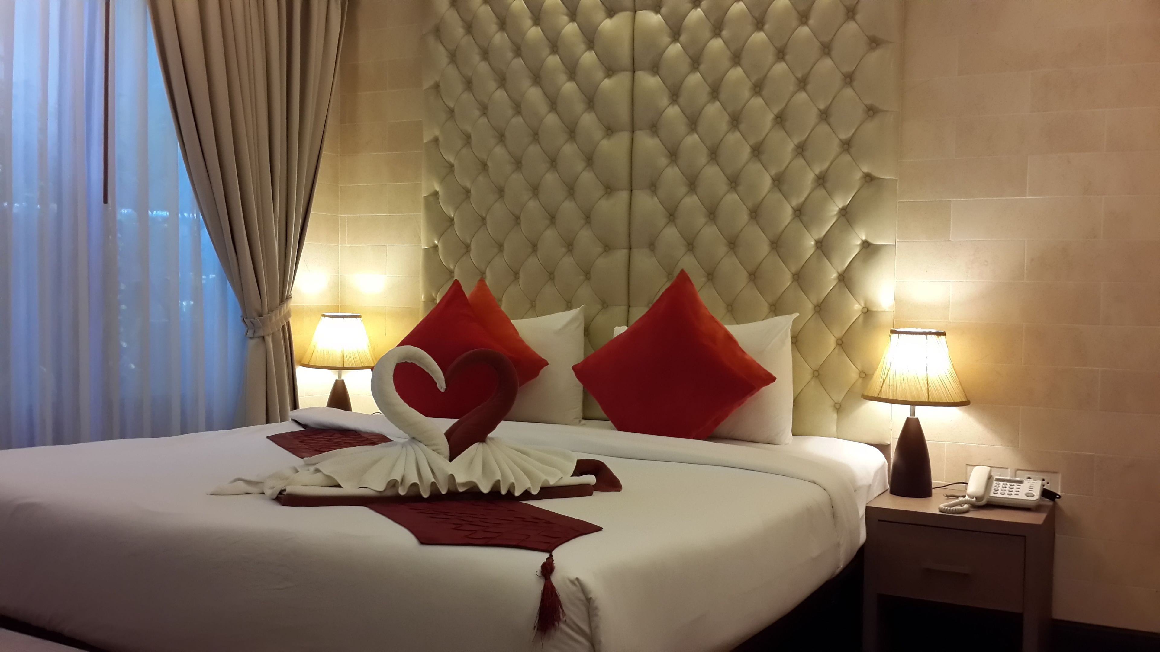 A hotel room with a large bed, a tufted headboard, two bedside lamps, and a telephone on the nightstand.