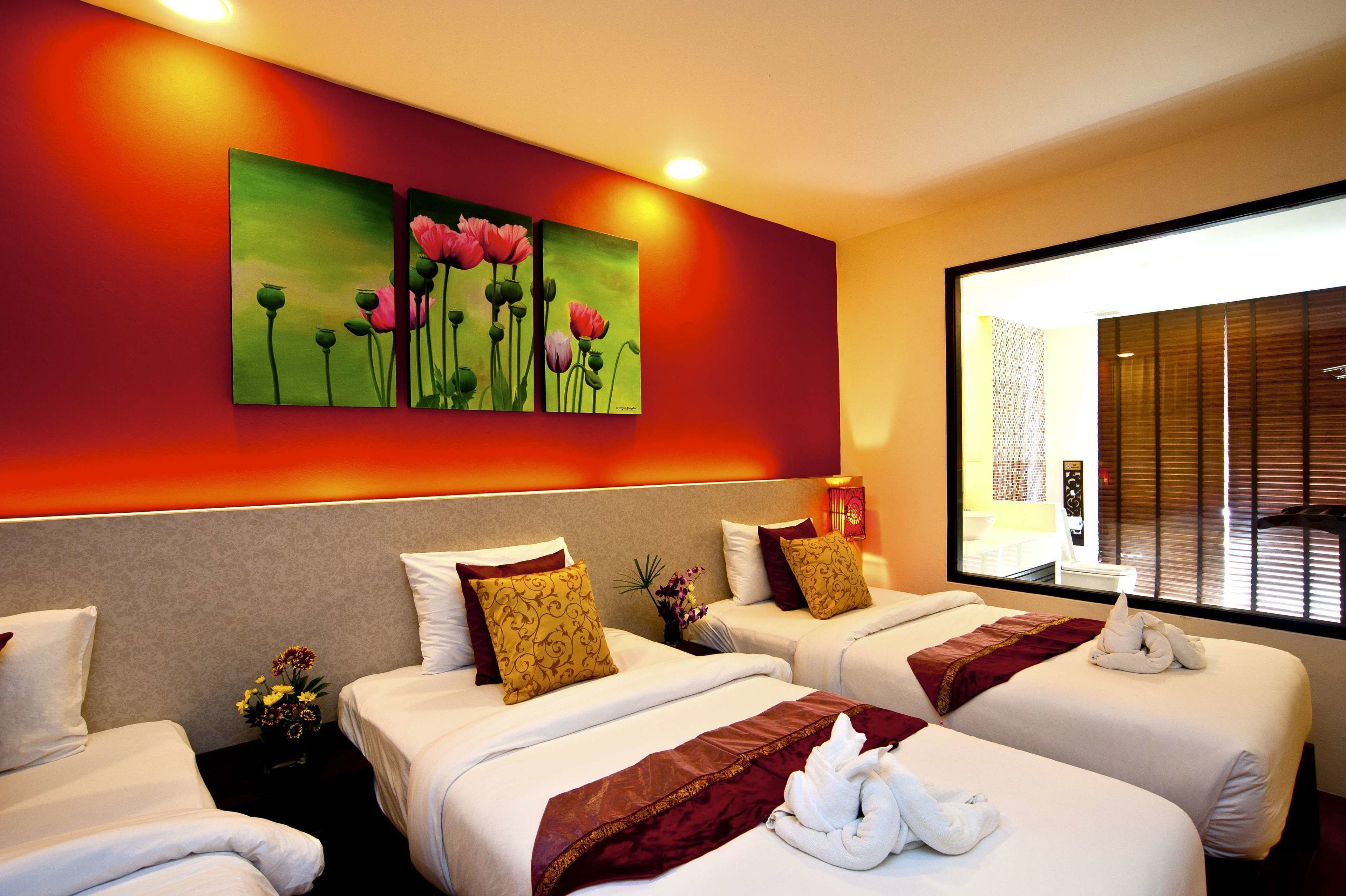 Une chambre d’hôtel avec deux lits, chacun agrémenté de draps blancs et de coussins décoratifs. Un tableau représentant des fleurs est accroché au mur au-dessus des lits, et une fenêtre avec des stores se trouve sur le côté droit.