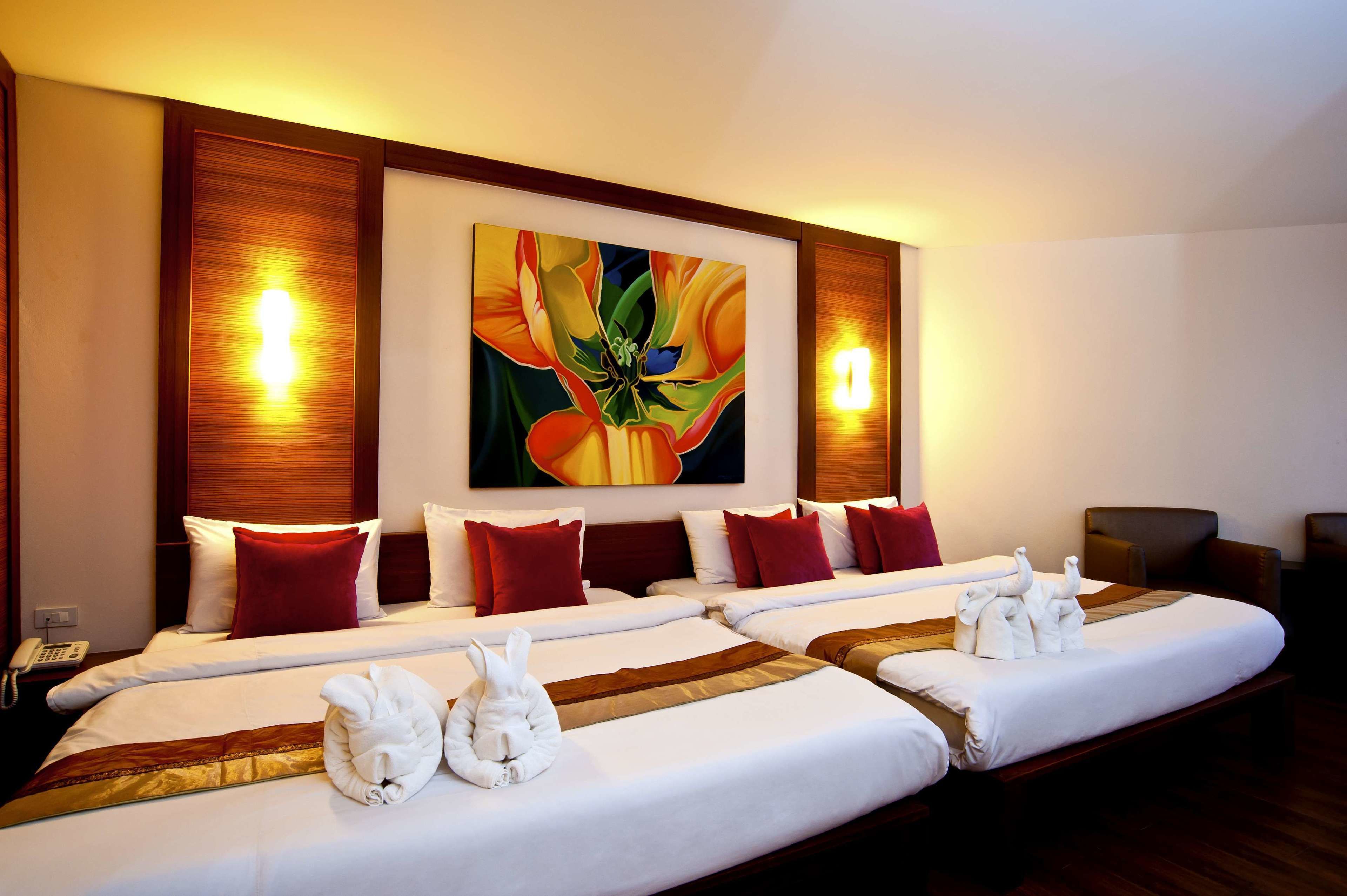 Habitación de hotel con dos camas, ropa de cama roja y blanca, una gran obra de arte floral sobre las camas y un teléfono en la mesita de noche.