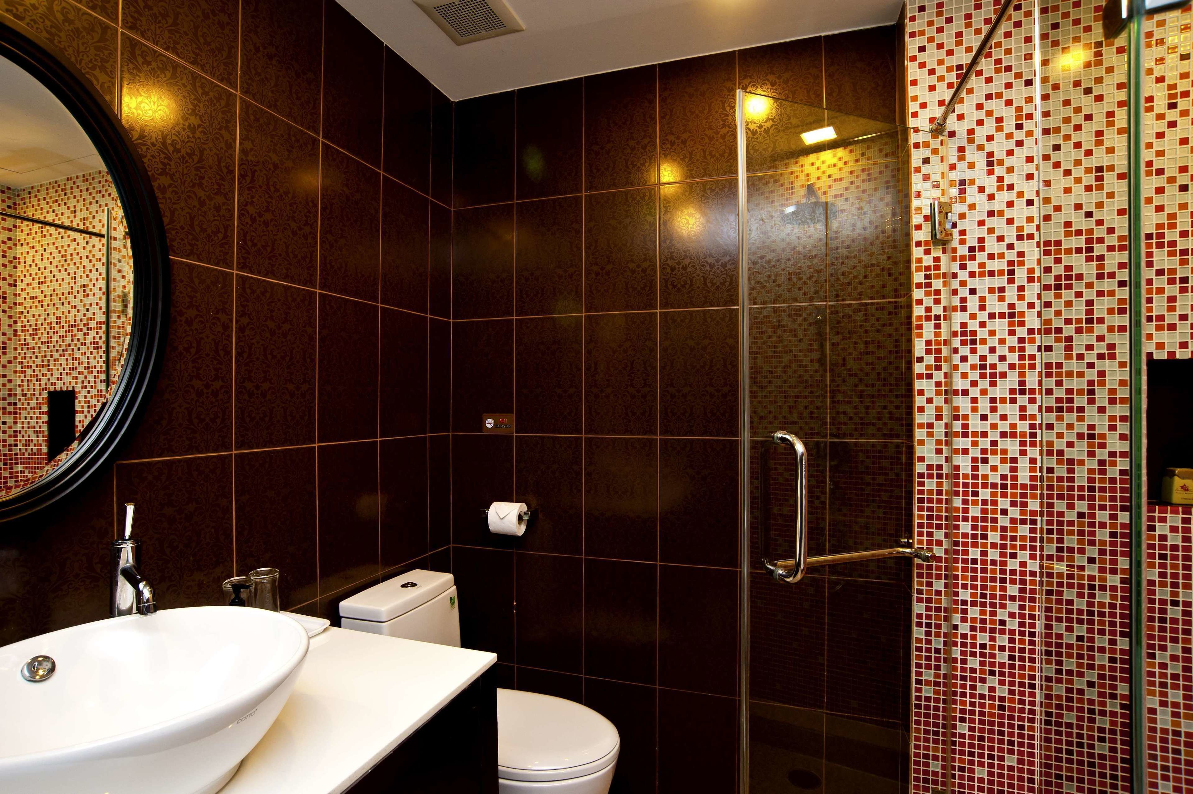 Ein Badezimmer mit rundem Spiegel, Waschbecken, Toilette und Duschbereich mit Fliesenwand.