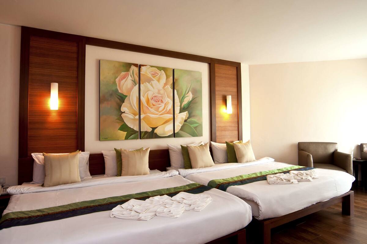 A hotel room with two beds, a large floral painting on the wall, and two wall-mounted lights.
