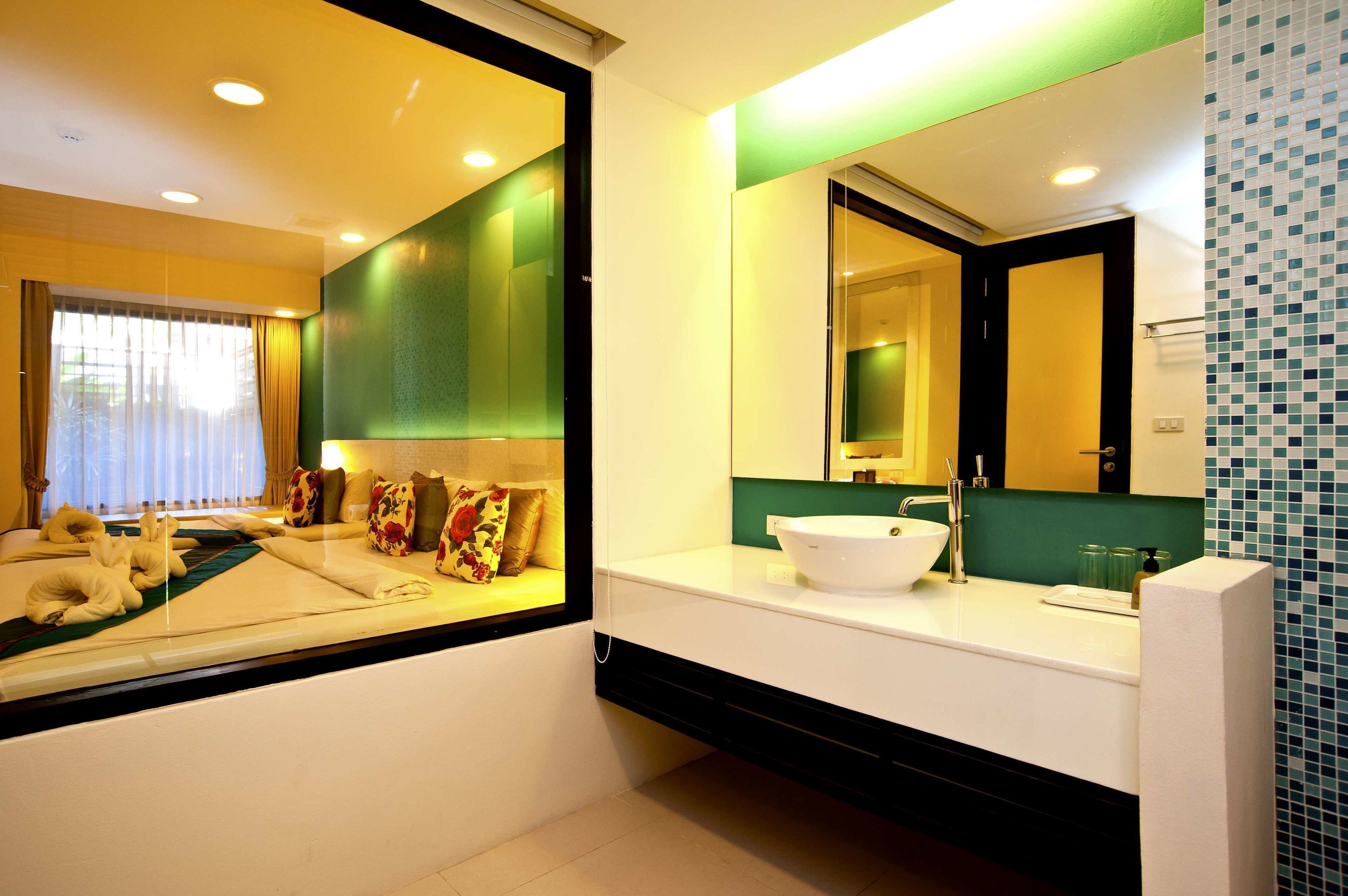 A modern bathroom with a large mirror, a white sink, and a green accent wall.