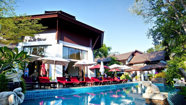 Un hotel moderno con piscina, sillas de lounge rojas y sombrillas.