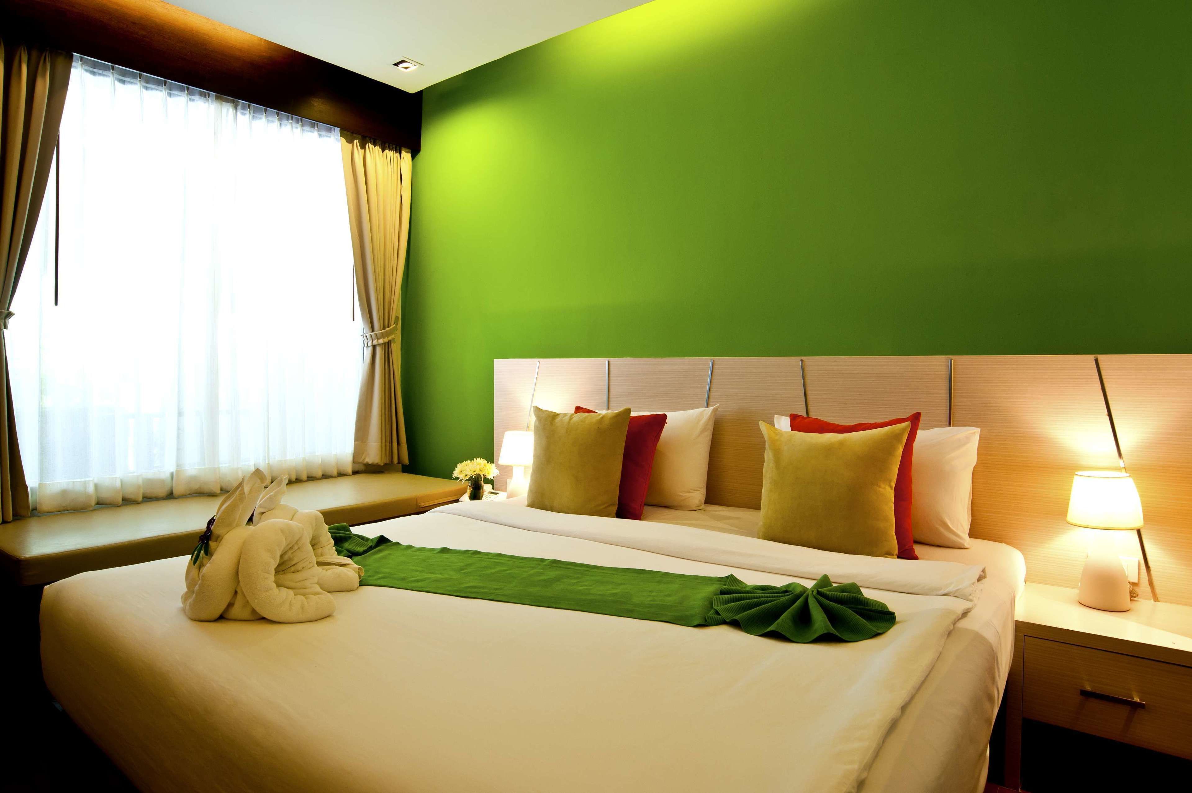 A hotel room with a bed, pillows, a bedside lamp, and a window with curtains.