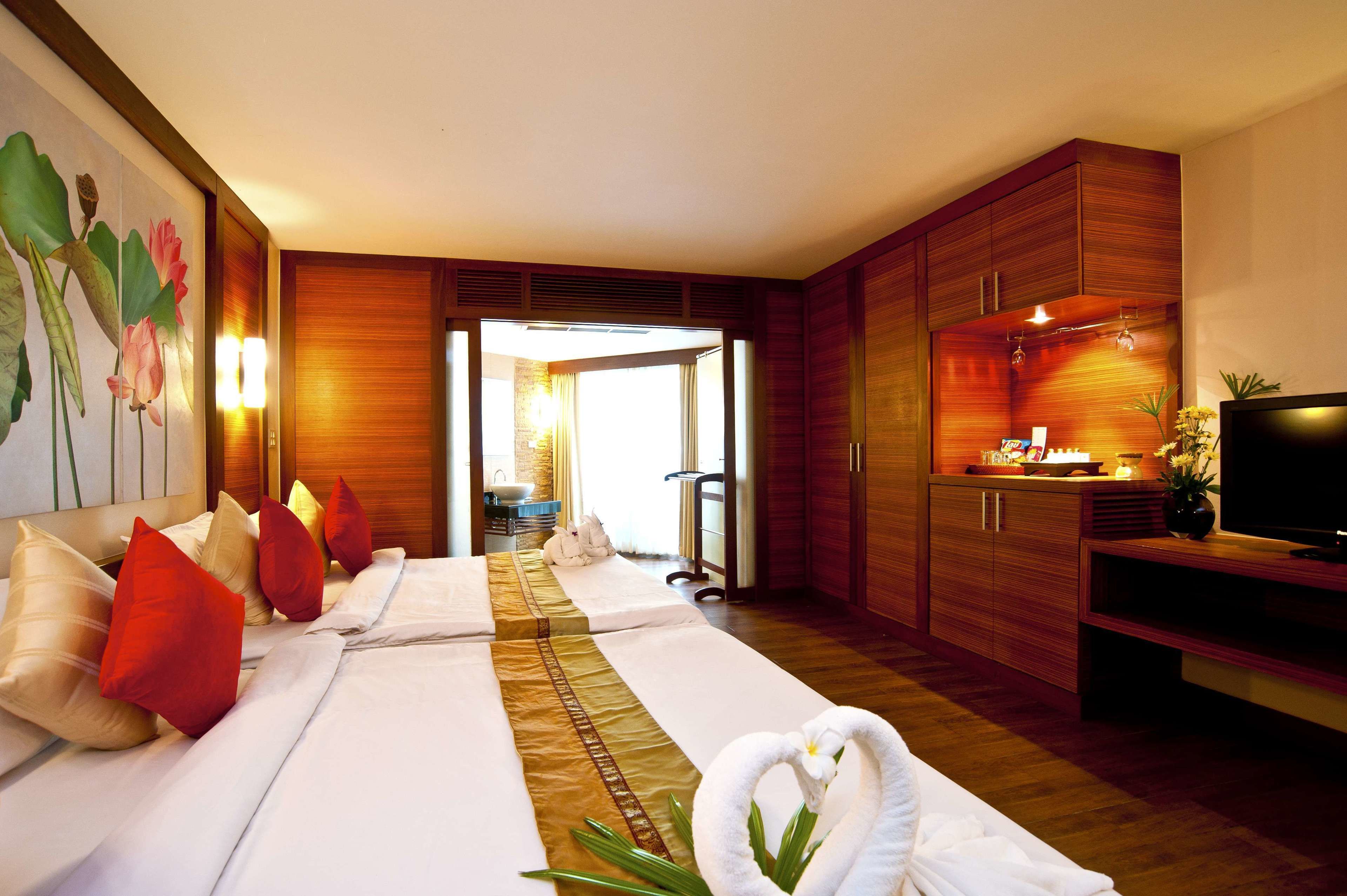 A hotel room with a large bed, wooden cabinets, a television, and a bathroom visible through an open door.