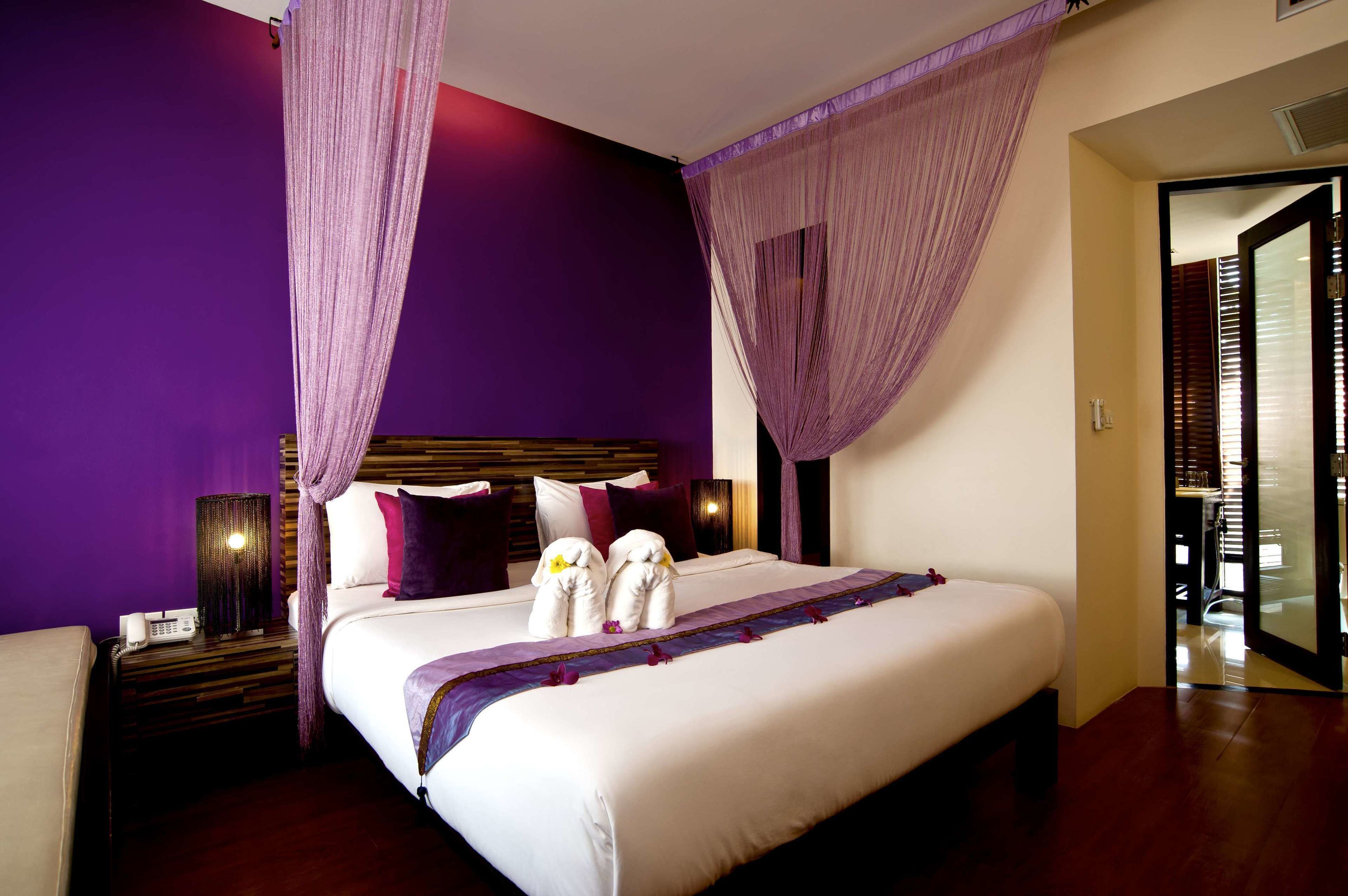 Una habitación de hotel con una cama grande, paredes moradas y un dosel.