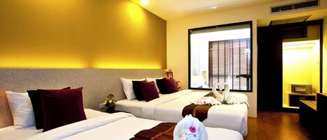 A hotel room with two beds, a large window with blinds, a bedside table with a lamp, and a TV.