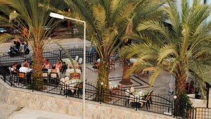 An outdoor seating area with palm trees, tables, and chairs. - Sailor Apart Hotel (Alanya)