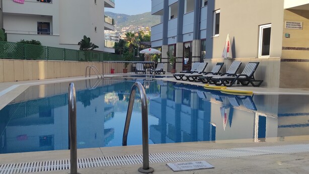A swimming pool with lounge chairs and a safety sign. - Sailor Apart Hotel (Alanya)