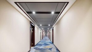 Un long couloir avec un tapis à motifs, des luminaires encastrés et des portes de part et d’autre.