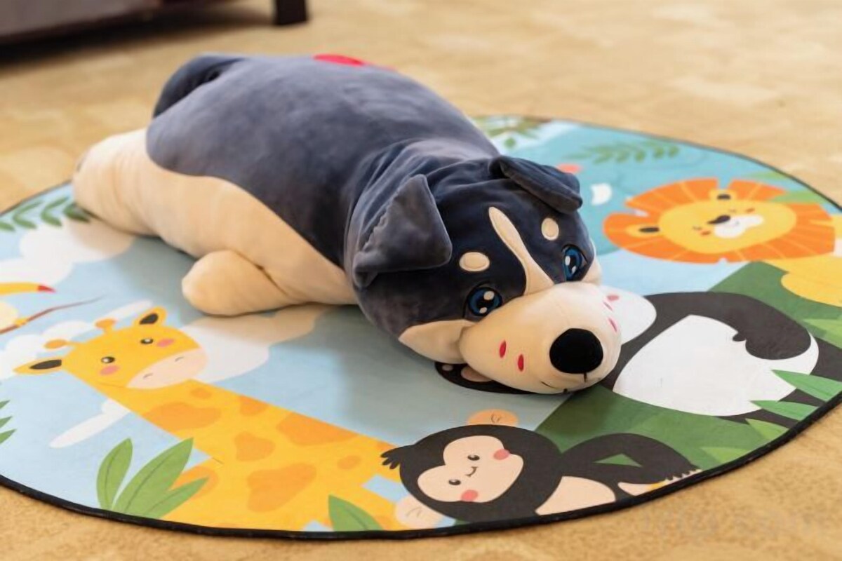 A plush toy on a colorful mat with animal and cartoon characters.