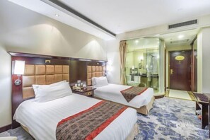 Two beds with tufted headboards, a bedside table, and a glass-enclosed bathroom.
