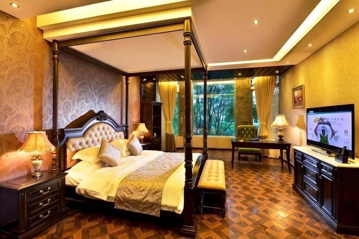A four-poster bed with a canopy, a television, and a desk with a chair in a hotel room.