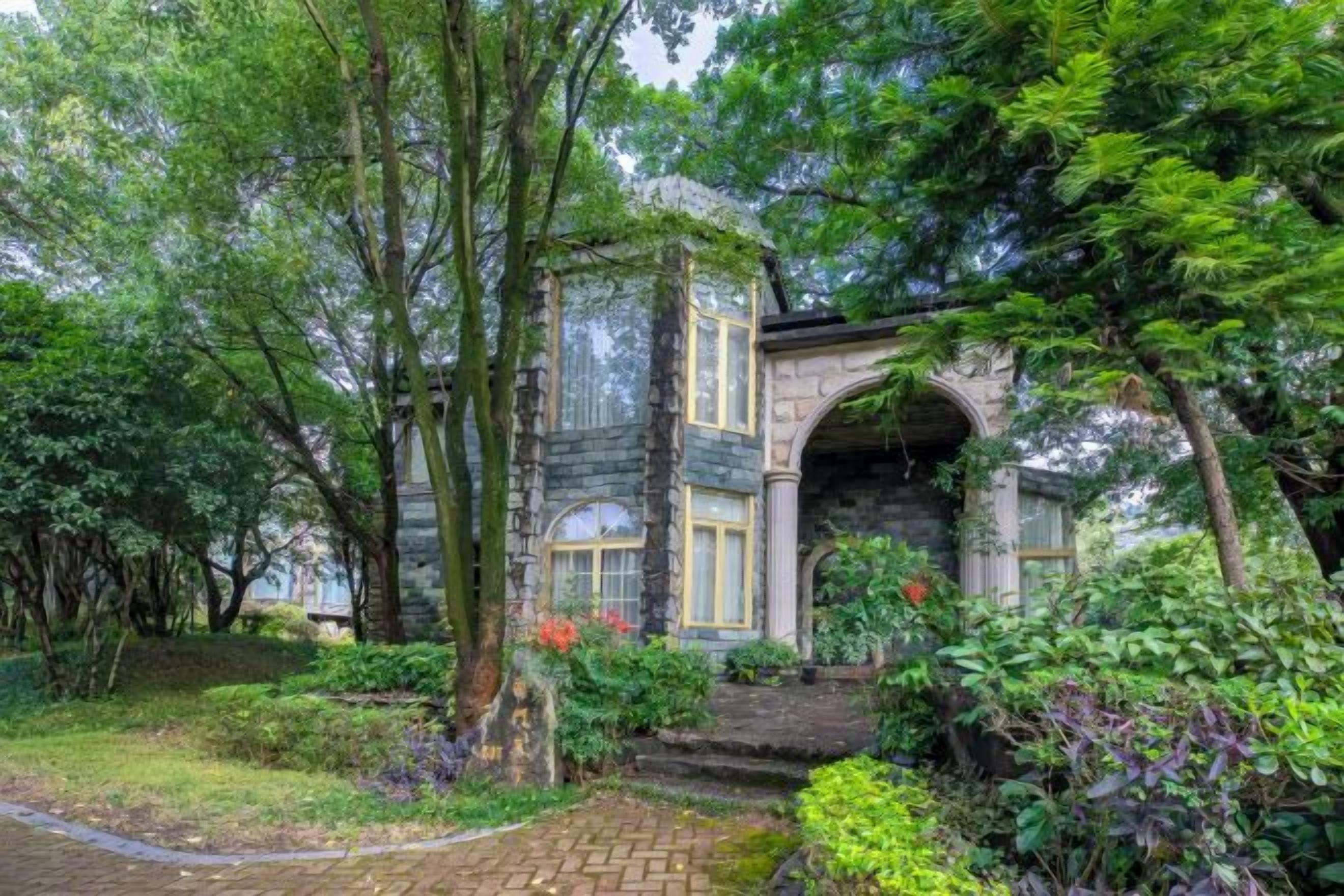 A stone building with a large arched entrance, surrounded by lush greenery and a brick pathway.