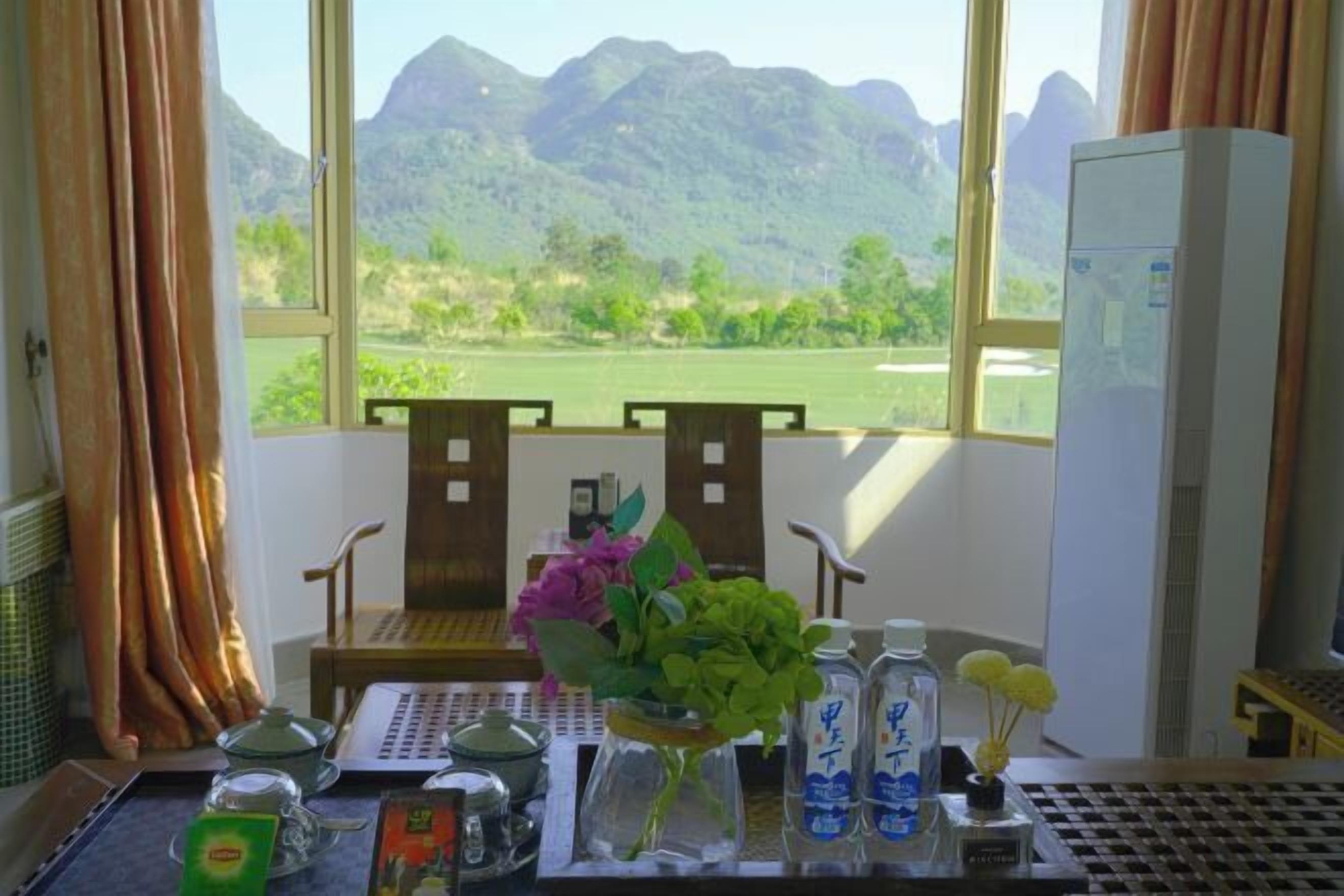 A room with a view of mountains, a desk with a vase of flowers, a water bottle, and a small cabinet.