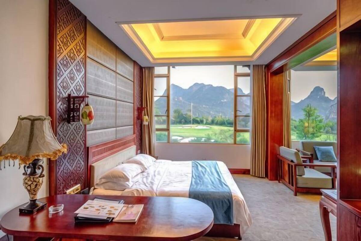 A hotel room with a bed, a desk, a chair, and a view of mountains.