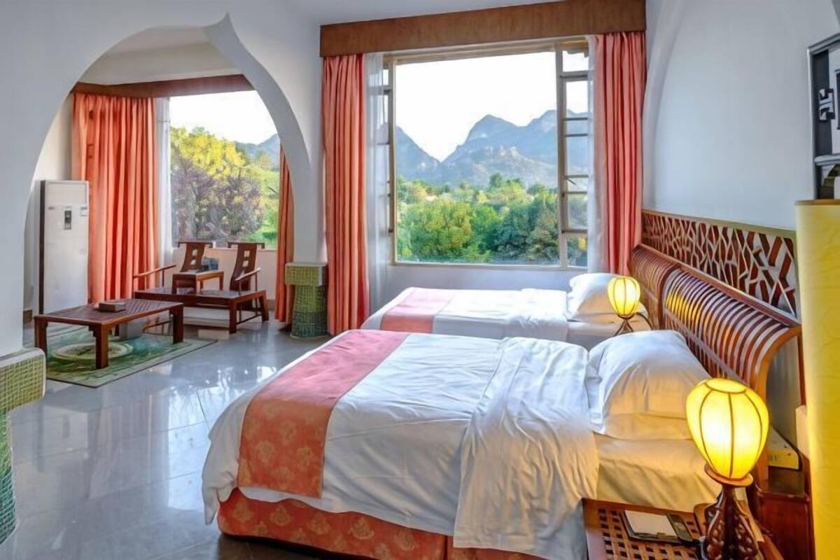 A hotel room with two beds, a desk, and a view of mountains.