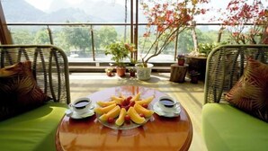 Une table avec des fruits et du café sur un balcon, agrémenté de meubles en osier et offrant une vue sur les montagnes.