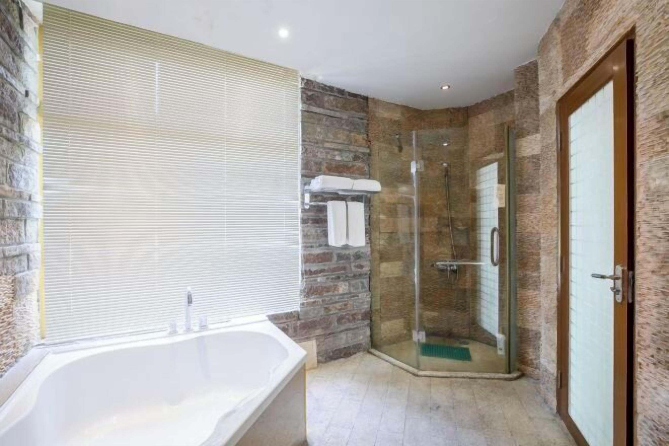Un baño con bañera, ducha con cerramiento de vidrio, paredes de piedra y puerta de madera.