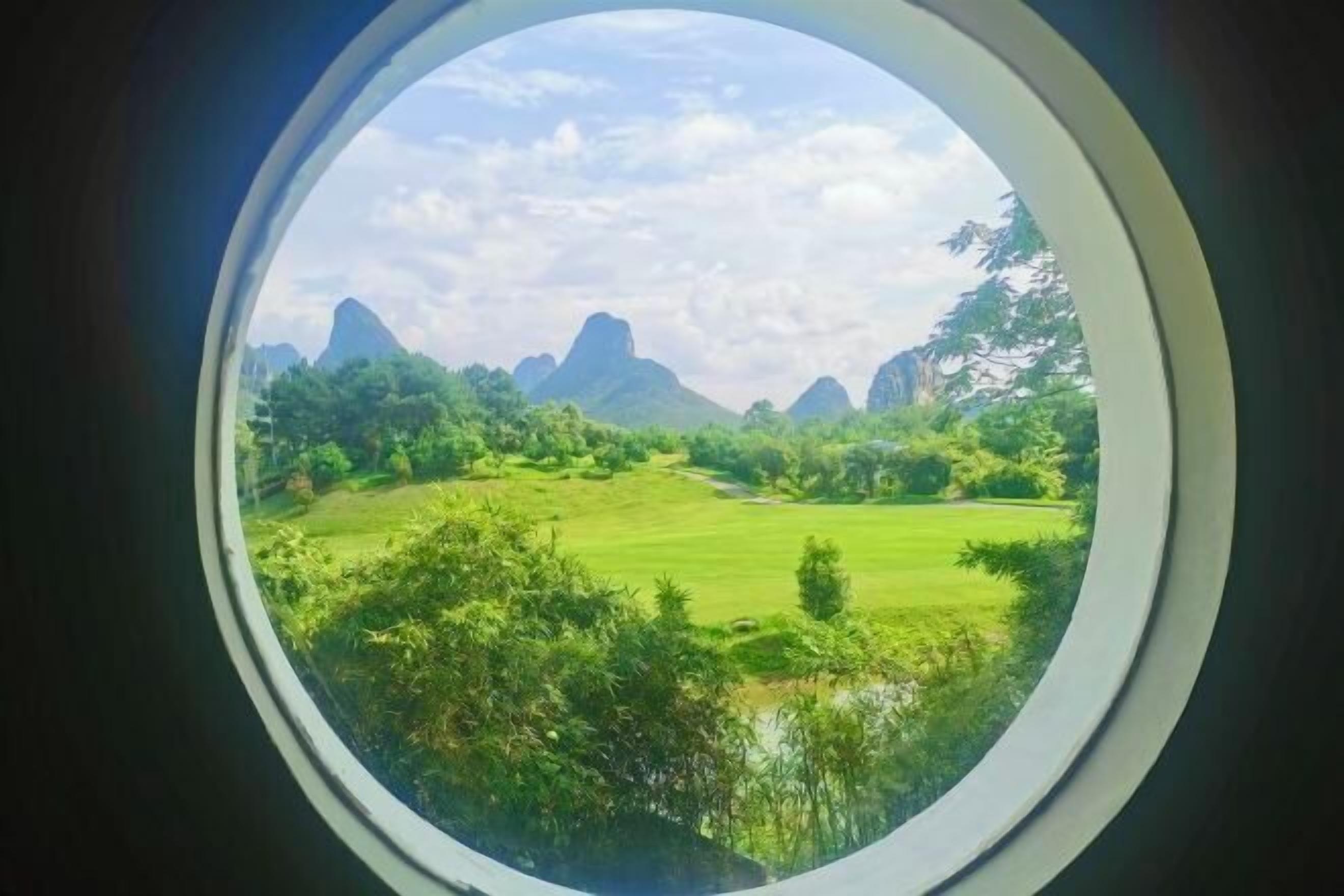 Une fenêtre ronde offre une vue sur un paysage de montagnes et de verdure.