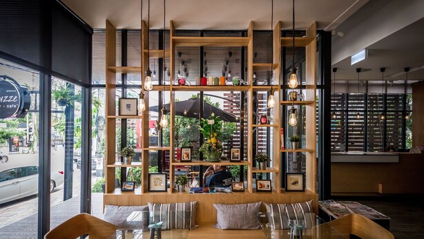 A modern cafe with a wooden bookshelf, seating area, and large windows. - Mooks Residence (Pattaya)