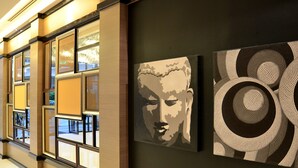 A hallway with framed artwork on the walls, a window with a view of the outdoors, and a tiled floor. - Mooks Residence (Pattaya)