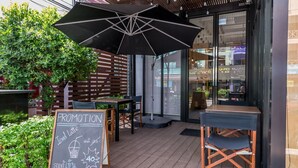 An outdoor seating area with a wooden deck, a black umbrella, and a chalkboard sign advertising a promotion for iced lattes. - Mooks Residence (Pattaya)