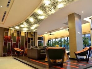 Eine moderne Lobby mit gewölbter Decke, einer Sitzecke mit Ledersesseln, einem Sofa und einem großen Fenster mit Blick auf Palmen.