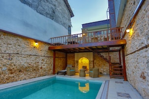 A stone-walled pool area with a wooden deck and lounge chairs.