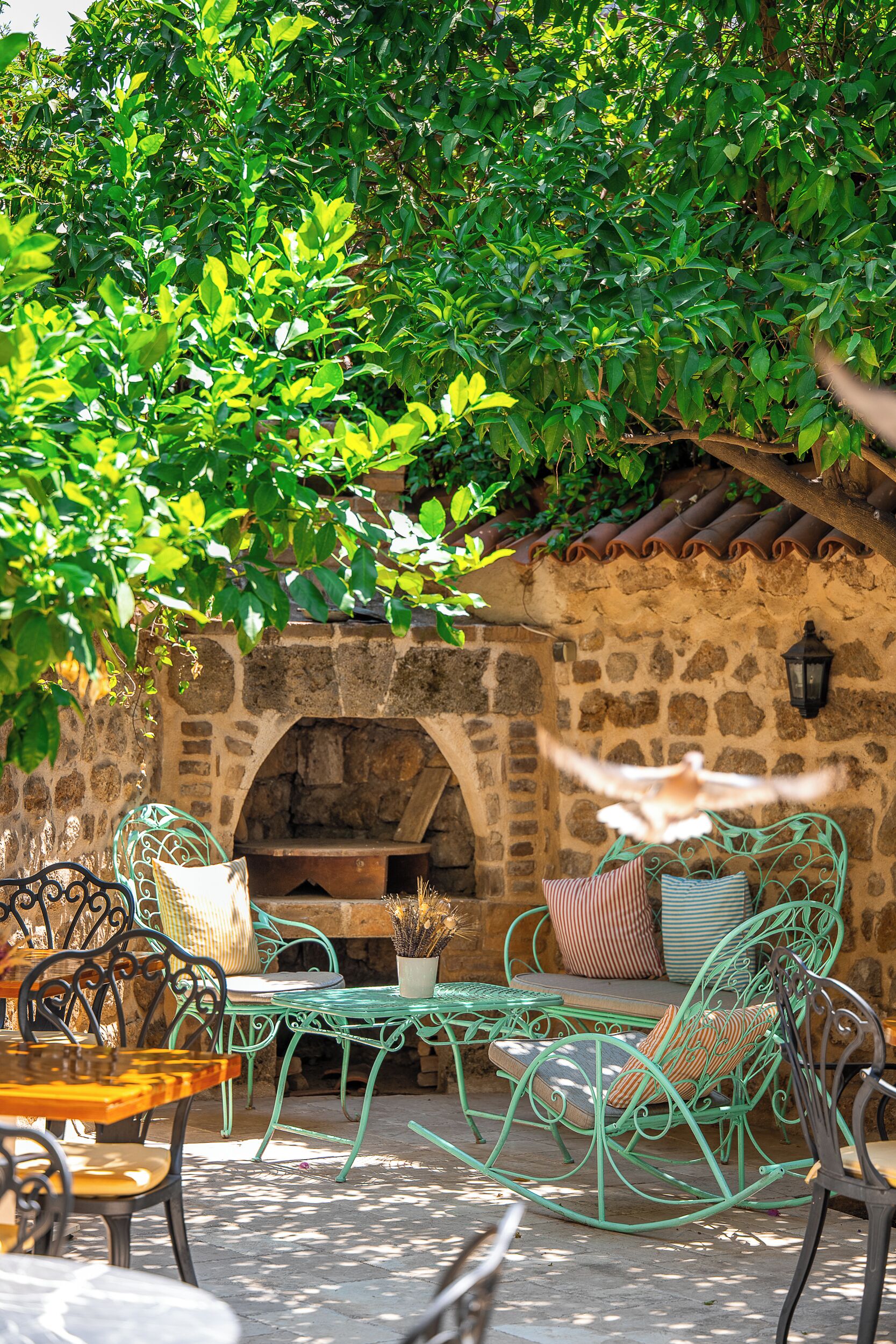 An outdoor seating area with metal chairs and tables, a stone wall, and a brick oven.