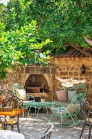 An outdoor seating area with metal chairs and tables, a stone wall, and a brick oven.