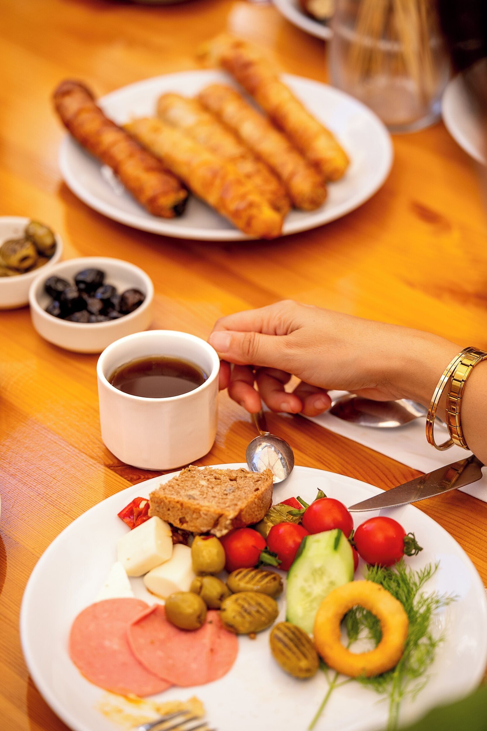 Una mesa de comedor con platos de comida, una taza de café y una mano sosteniendo una cuchara.