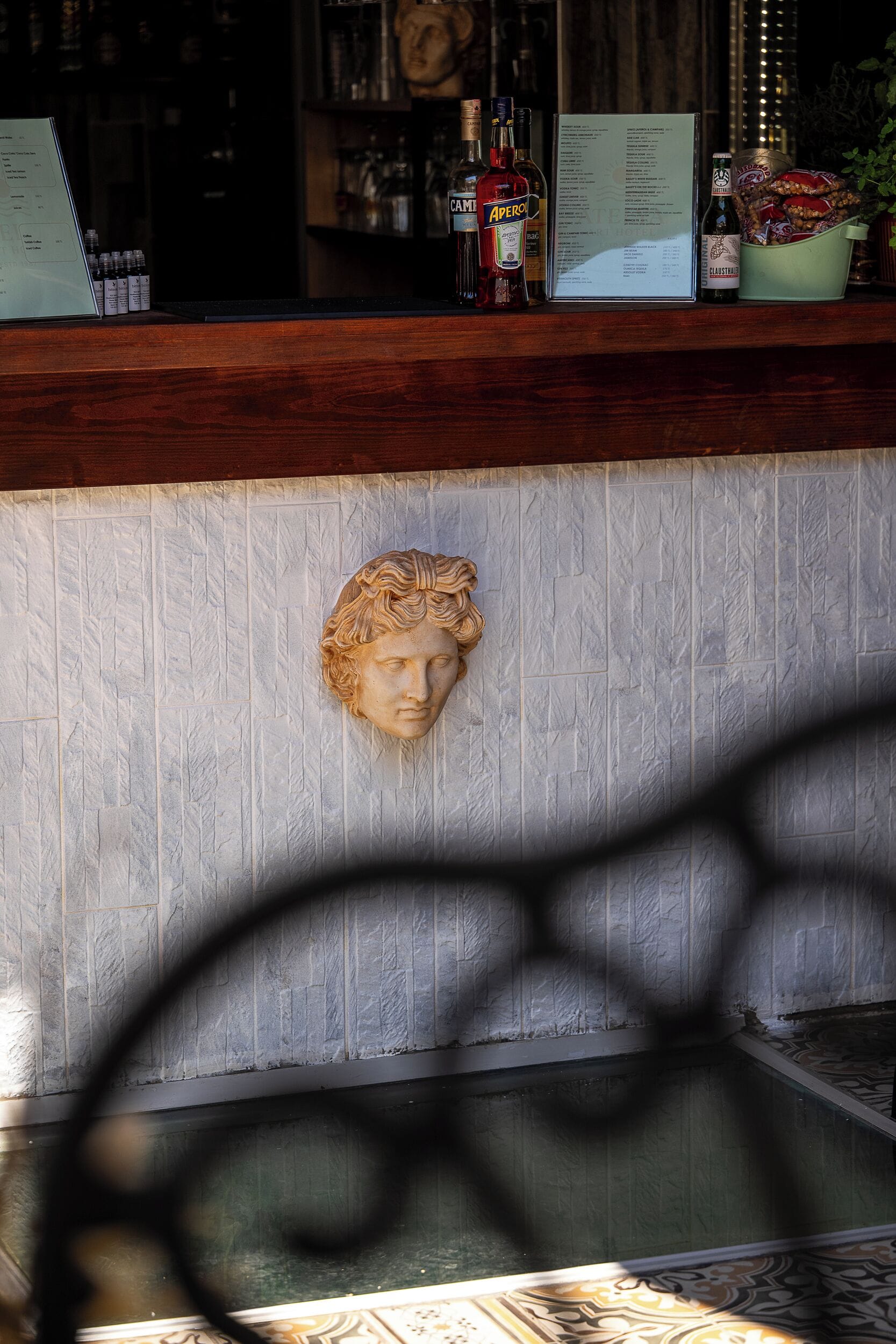 A bar area with a stone wall, a wooden counter, and various bottles and glasses.