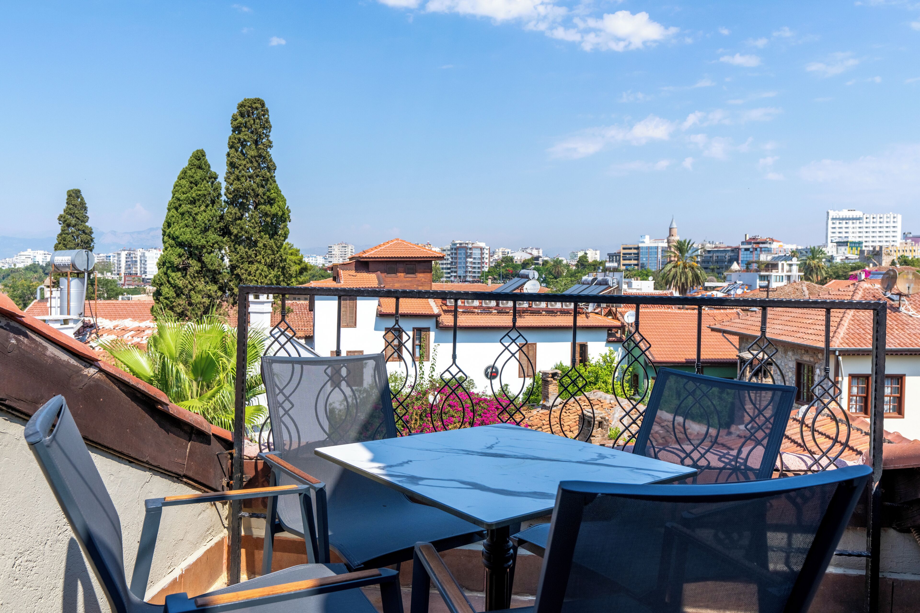 Terraza en la azotea con una mesa y sillas, con vistas a un paisaje urbano con edificios y árboles.