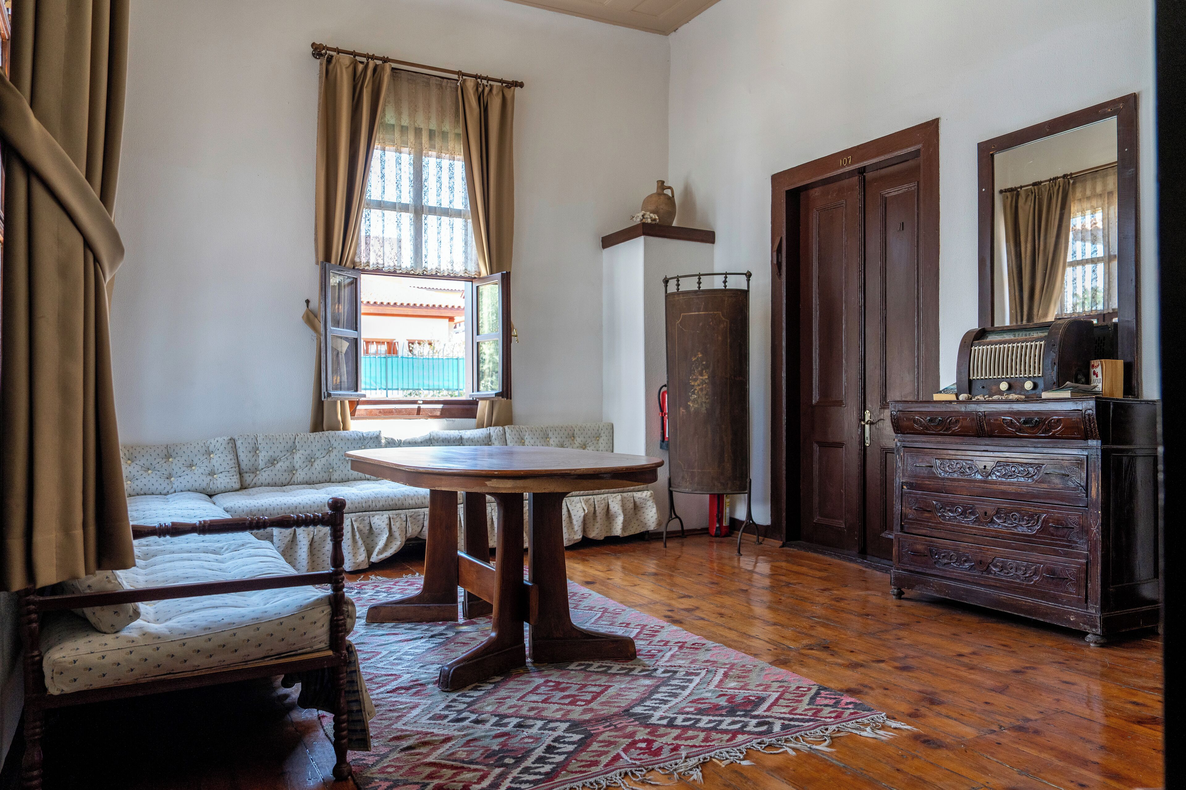 A room with a wooden floor, a round table, a sofa, a dresser, and a window with curtains.