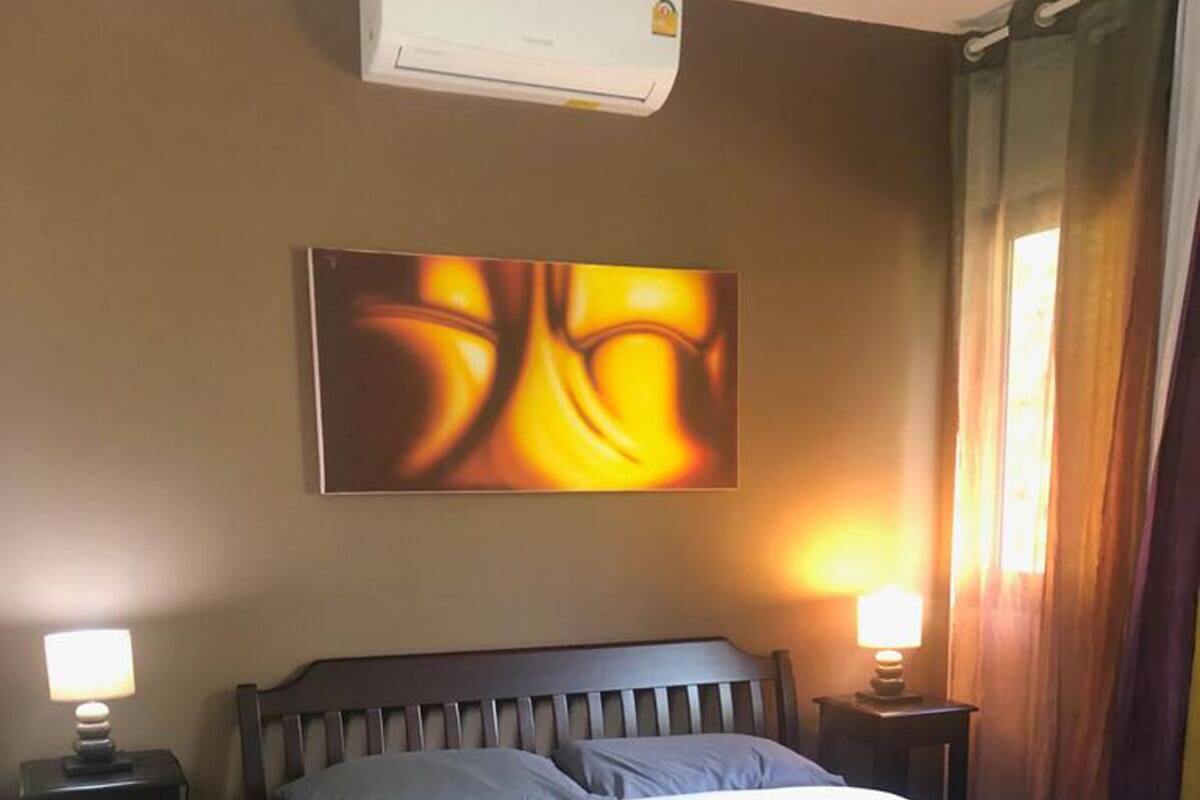 A bedroom with a bed, two bedside tables, a wall-mounted air conditioner, and a window with curtains.