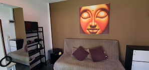 A hotel room with a bed, a TV, a shelf with items, and a painting on the wall.