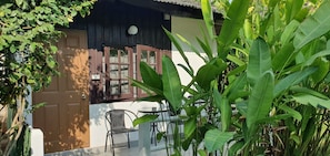 A house with a closed wooden door, a window with a white blind, and a small table with a chair outside.