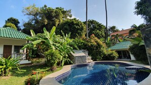 A swimming pool with a tiled edge, surrounded by lush greenery and a house with a green roof. - Green Canyon Resort (Koh Samui)