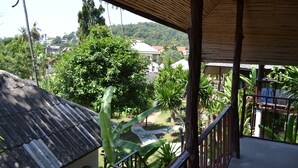 A balcony with a view of a lush garden, a wooden railing, and a building with a tiled roof in the background. - Green Canyon Resort (Koh Samui)