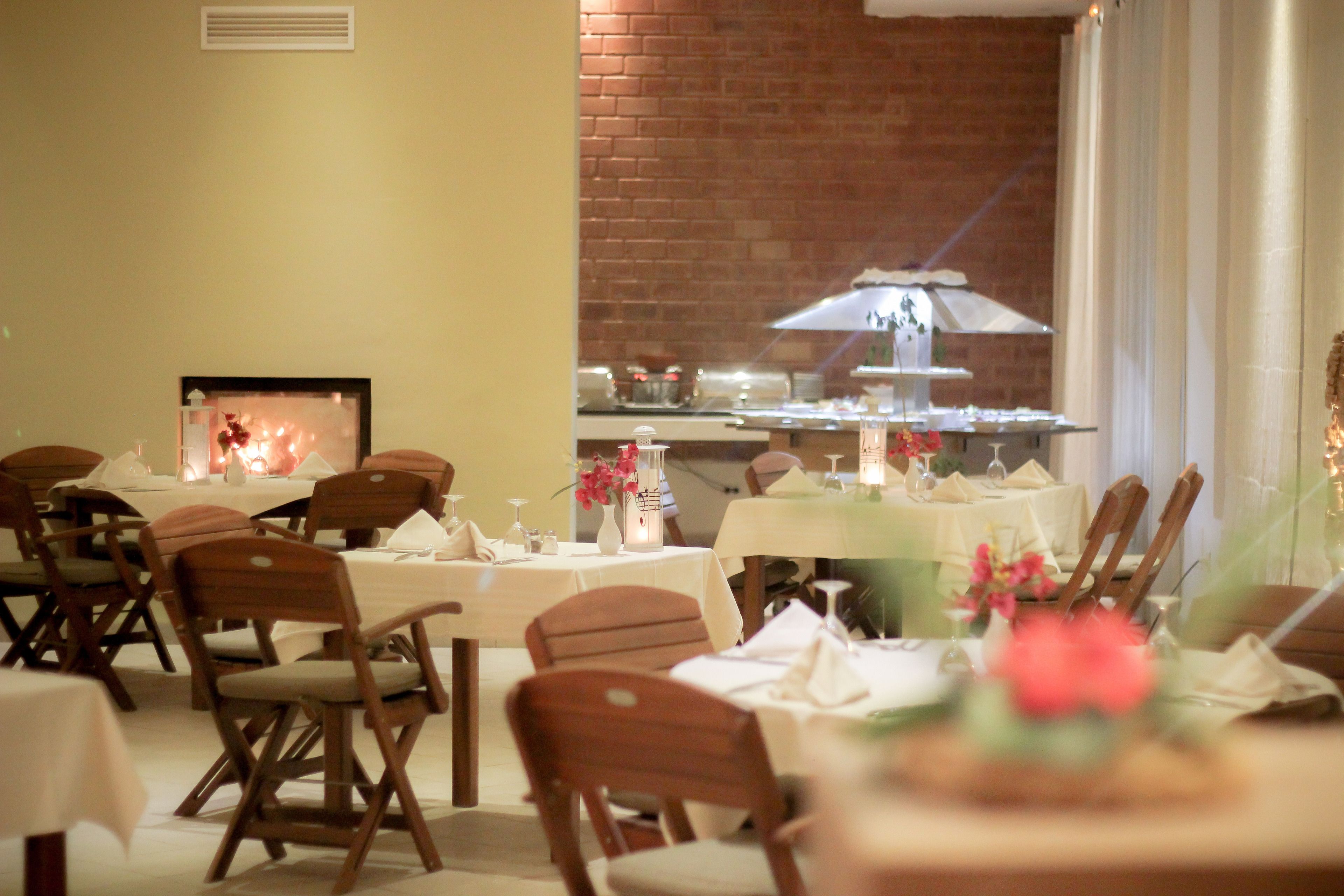 A restaurant with multiple tables set for dining, wooden chairs, and a brick wall in the background.