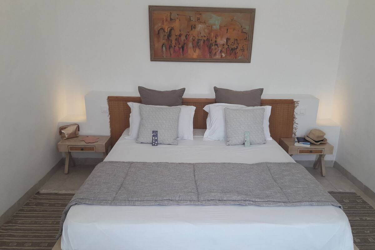 A neatly made bed with a grey blanket, two bedside tables with lamps, and a painting on the wall.