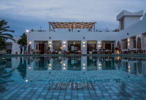 A pool area with a pergola, outdoor seating, and a building with multiple windows. - Les Jardins De Toumana (Djerba Midun)