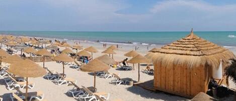 A beach with sun loungers and thatched umbrellas.