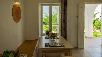 Un coin repas avec une table dressée pour deux personnes, un panier de fruits et une vue sur la verdure environnante.
