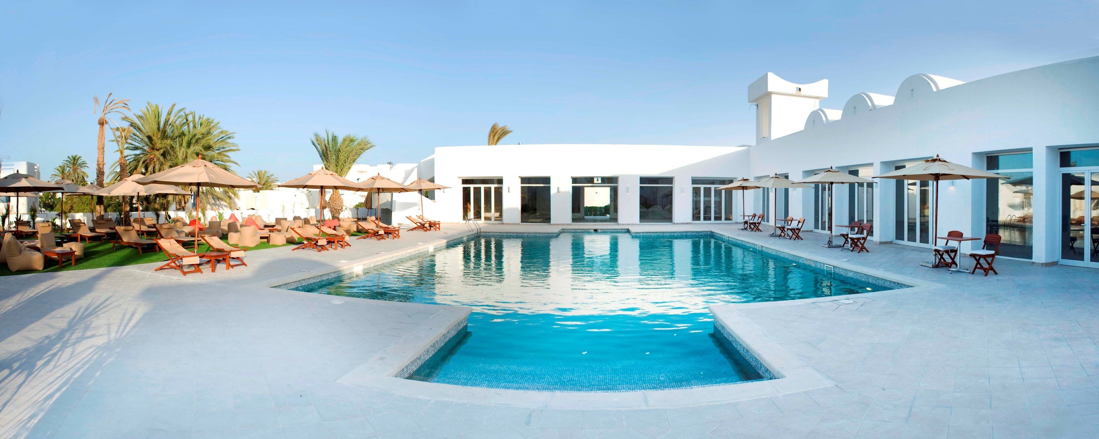 Una piscina al aire libre, sombrillas, sillones reclinables de piscina